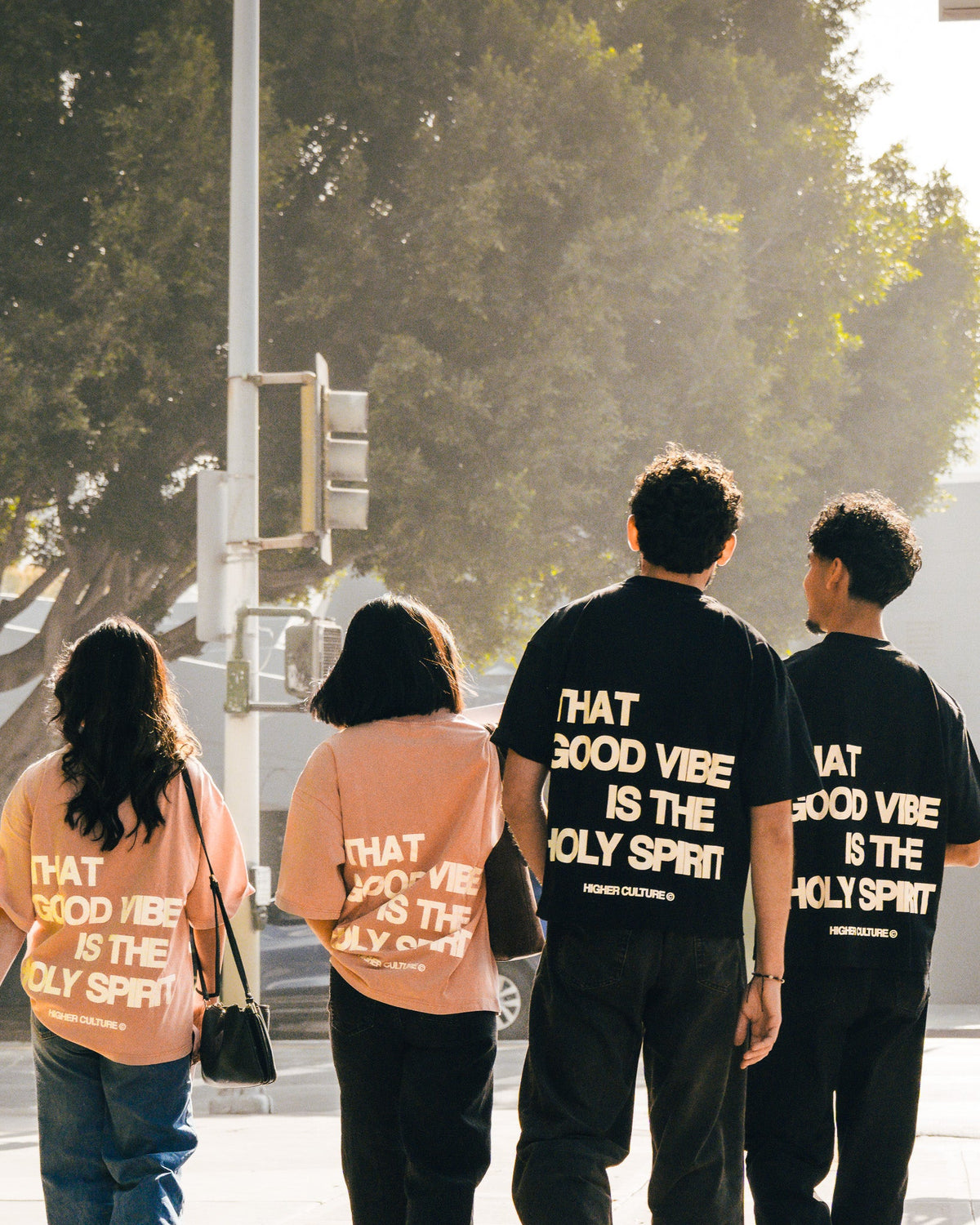 Three people walking in a city wearing black and peach graphic t-shirts with text.