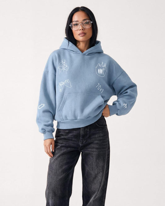 Woman wearing a blue oversized hoodie with white line art graphics and black jeans.